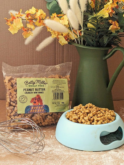 A bag of wheat-free peanut minis dog treats next to a bowl filled with the treats, with decorative flowers in the background.